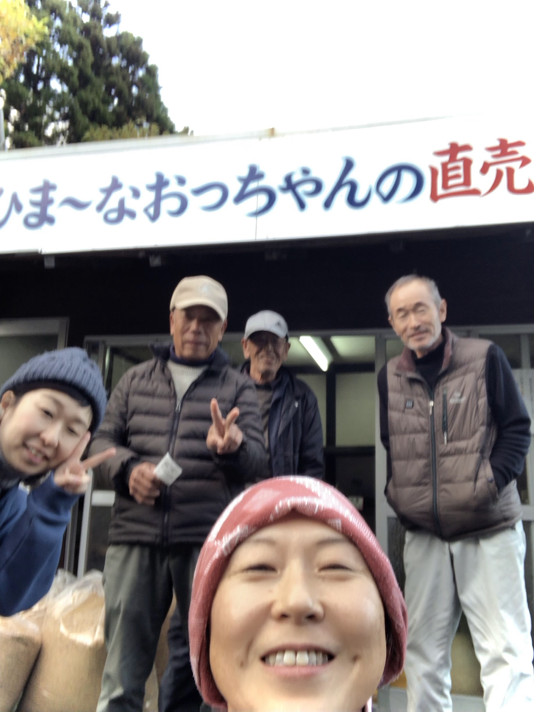 直売所の看板の下に5人全員が集まった記念の自撮り