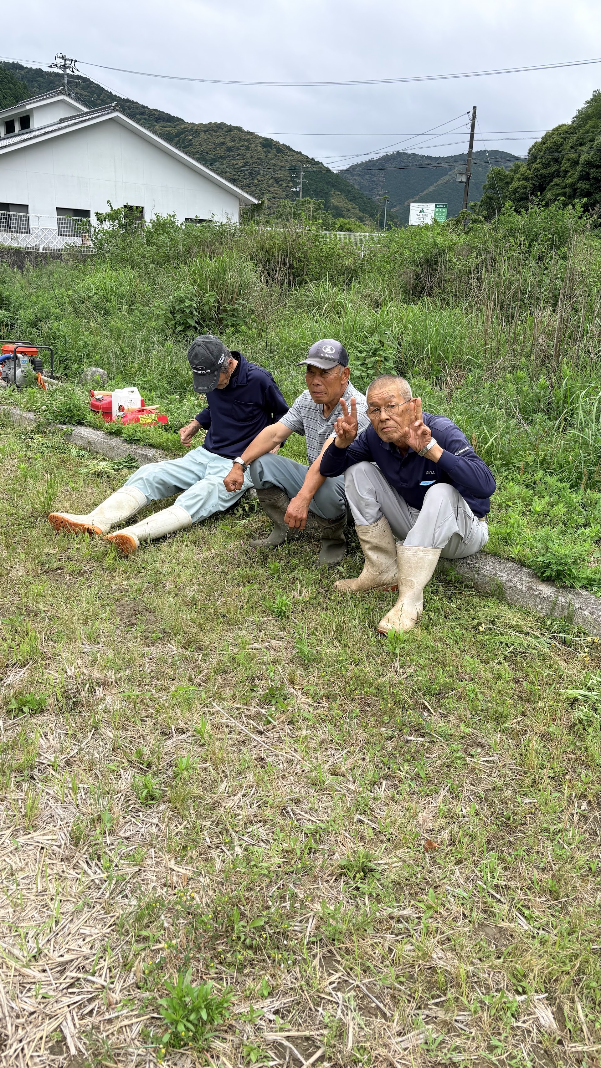 畑のあぜに並んで座ってピースする後期高齢者なかよし3人組